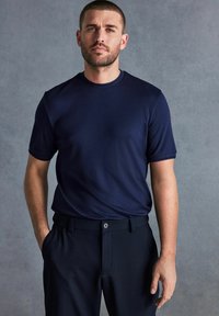 Marineblauw shirt met korte mouwen en een ronde halslijn, gemaakt van een gladde stof, gecombineerd met donkere broeken met een knoopdetail.