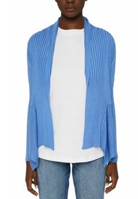 Kvinna iklädd en blå ribbad cardigan med öppen framsidan över en vit skjorta och blå jeans, med avslappnade ärmar och en draperad passform.