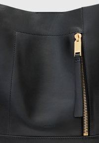 Czarna skórzana torba z wyraźnym złotym zapięciem, gładką teksturą i minimalistycznym widokiem szwów, z jedną kieszenią z przodu.