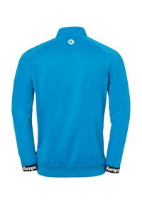 Blå træningsjakke med høj krave, lange ærmer, elastiske manchetter og en sort kant i nederste del, der har "Kemp" logo. Glat tekstur.
