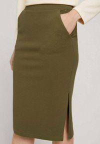 Jupe longueur genou vert olive en tissu texturé, avec poches latérales et une fente au dos pour faciliter les mouvements.