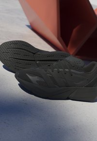 Black athletic shoes with a textured upper, mesh detailing, and rubber soles. Features prominent branding and a streamlined design.
