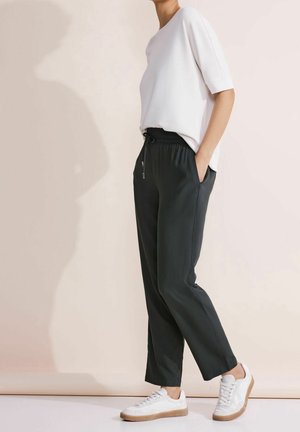 Witte top met korte mouwen in een ontspannen pasvorm, gecombineerd met donkergrijze elastische broek met zijzakken en witte sneakers met tan kleurige zolen.