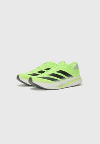 Neon groene hardloopschoenen met zwarte strepen, lichtgewicht ontwerp, gestructureerde bovenkant en een grijze accenten op de hiel. Gevoerde witte zool.