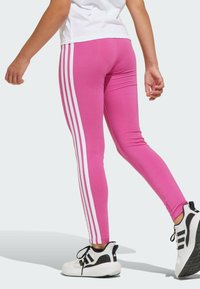 Leggings rosa aderenti in tessuto elastico, con strisce laterali bianche. Abbinati a scarpe da ginnastica nere e bianche.