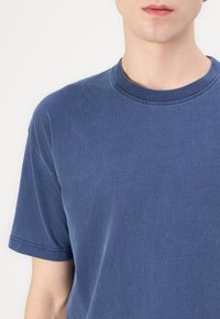 Blue crew-neck t-shirt in cotton blend, featuring short sleeves and a smooth texture, with visible stitching along the neckline.