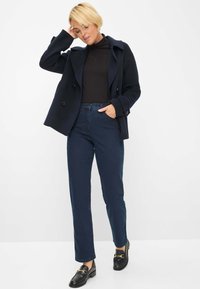 Marine peacoat met brede revers en dubbelknopen, gecombineerd met donkerblauwe jeans en zwarte instappers met gouden hardware accenten.