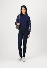 Mörkblå sweatshirt med blommönstrade ärmar, matchad med mörka skinny jeans och vita sneakers, accessoriserad med en grå axelväska.