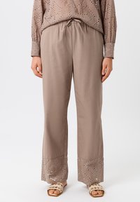 Pantalons marron clair en matériau doux avec une coupe décontractée, présentant des motifs découpés décoratifs au bas de l'ourlet.
