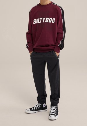 Mørkerød sweatshirt med "SALTY DOG" tryk, sorte accenter og hvide striber; parret med sorte bukser og sorte sneakers med hvide såler.