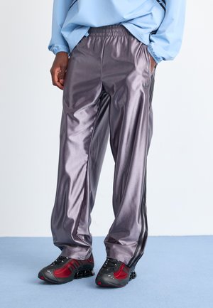 Metallic grey track pants with a relaxed fit, featuring black side stripes and an elastic waistband. Worn with black and red sneakers.