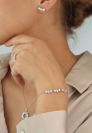 Silver jewelry set including stud earrings, a bracelet, and a necklace. Each piece features intricate designs with clear stone accents.