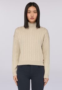 Beżowy sweter z dzianiny warkoczowej z golfem, z prążkowanymi mankietami i dołem. Miękka tekstura, krótki krój, z pionowym wzorem i bocznym logo.