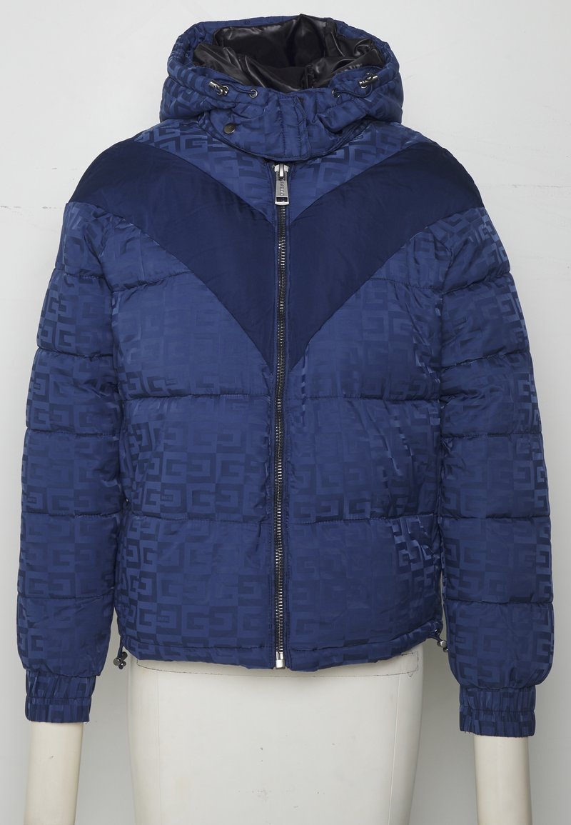 Doudoune bleu marine avec motif géométrique, fermeture éclair devant, poignets élastiques et capuche avec cordon sur un buste de mannequin blanc.