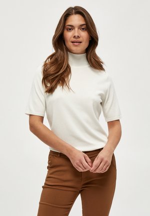Suéter blanco de cuello alto y manga corta hecho de una tela suave, con detalles acanalados en el cuello y las mangas, combinado con pantalones marrones.