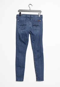 Mörkblå smala jeans hängande på en galge, med midjehöjd, bakfickor med dekorativt sömnad och en mjuk denimtextur.