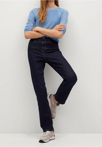 Lichtblauwe, getextureerde trui, donkerblauwe, hooggehate jeans en grijze sneakers. De jeans hebben een rechte pijp en lichte vervaging.