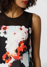 Haut sans manches à motif floral avec un col en maille noire. Il présente un imprimé floral vivant dans des nuances de rouge, rose et blanc sur un fond noir.