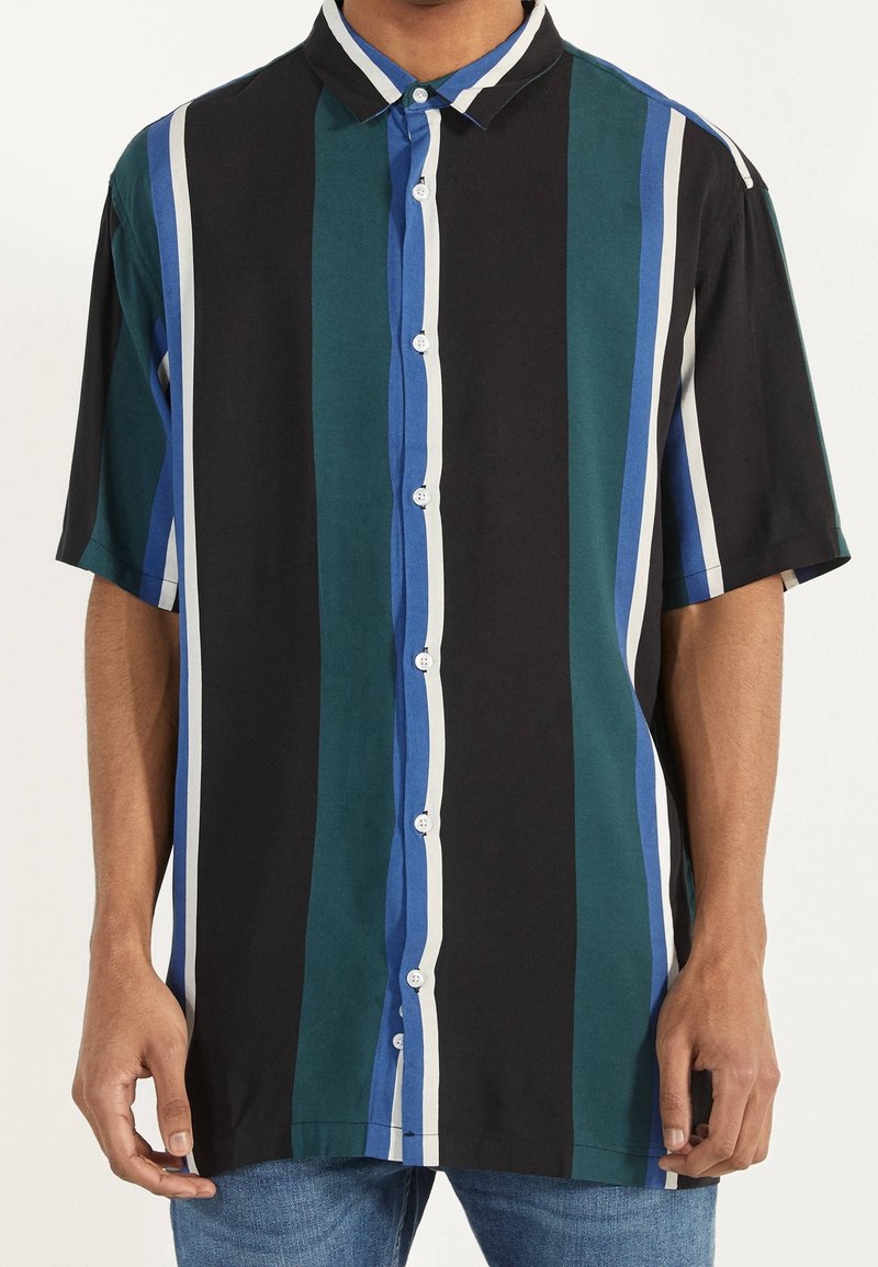 Camicia a maniche corte con righe verticali in nero, teal e blu con dettagli bianchi. Realizzata in tessuto liscio, design con bottoni frontali.