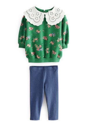 Grøn langærmet bluse med blomstermønster og stor hvid bølget krave, kombineret med ensfarvede blå tætsiddende leggings.