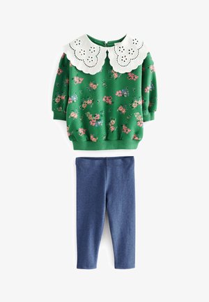 Grøn langærmet bluse med blomstermønster og stor hvid bølget krave, kombineret med ensfarvede blå tætsiddende leggings.