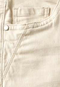 Beżowa bawełniana tkanina o diagonalnej strukturze prążków, z przednią kieszenią i srebrnym guzikiem oraz kontrastowym beżowym przeszyciem.