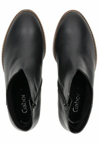 Botas de cuero negro hasta el tobillo con un acabado suave, punta redondeada, cremalleras laterales y costuras marrones contrastantes en el borde de la suela.