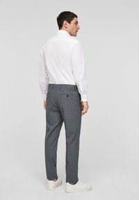 Grijze geruite broek met een slim fit, voorzien van achterzakken en een subtiele textuur, gecombineerd met een wit shirt en witte sneakers.