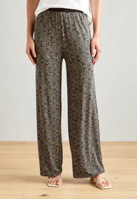 Pantalons à jambes larges en tissu léger, avec un motif abstrait noir et crème, une taille élastique et une coupe décontractée.