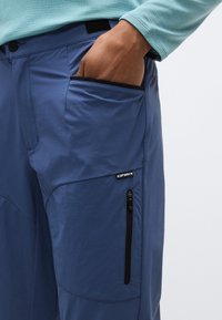 Μπλε παντελόνια πεζοπορίας από ελαφρύ ύφασμα, με πλαϊνές τσέπες που κλείνουν με μαύρα φερμουάρ και κλείσιμο στη μέση με βέλκρο.