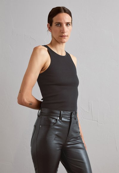 Débardeur noir à côtes associé à un pantalon en cuir noir taille haute. La tenue présente une silhouette ajustée et un design minimaliste.