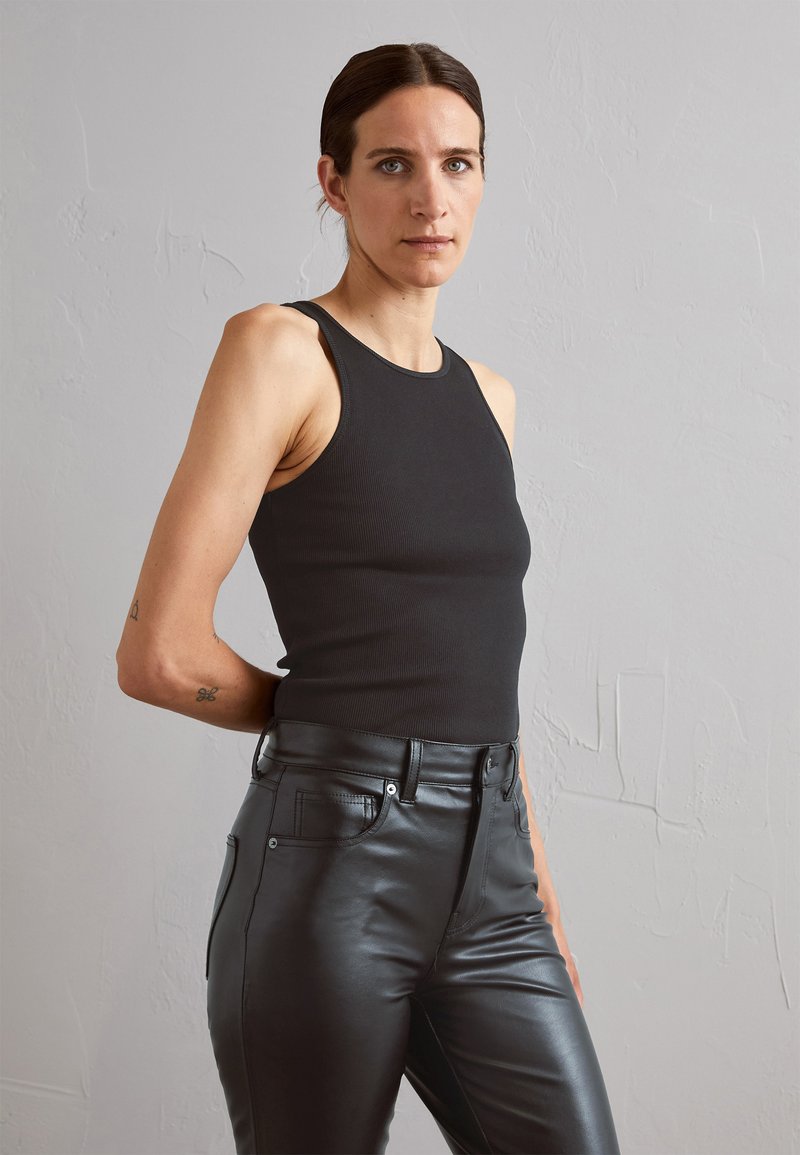 Black ribbed tank top paired with high-waisted black leather pants. The outfit has a fitted silhouette and minimalistic design.