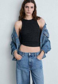 Top croptop negru cu nervuri, asortat cu o jachetă din denim albastru și blugi albaștri cu talie înaltă. Materialul pare moale și are un design ajustat.