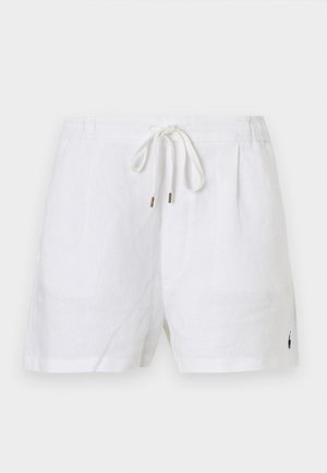 Γυναίκα που φοράει μπλε κοντομάνικο πουκάμισο με κουμπιά, λευκά σορτς, λευκά σανδάλια, κρατώντας μια πράσινη και κίτρινη πλεκτή τσάντα.