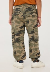 Pantaloni cargo mimetici in khaki e verde, con vita elastica, tasche laterali e fondo affusolato. Sneakers bianche visibili in basso.