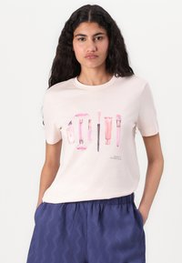 Lichtroze katoenen T-shirt met een gedrukt ontwerp van verschillende schoonheidsproducten in roze tinten. Ronde halslijn, korte mouwen en een losse pasvorm.