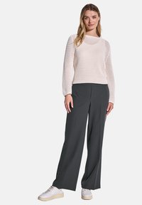 Helles rosa gestricktes Sweatshirt mit lockerer Passform und langen Ärmeln, kombiniert mit dunkelgrauen weit geschnittenen Hosen und weißen Sneakern.