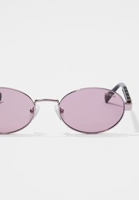 Oval sunglasses with purple tinted lenses, silver metal frame, and clear nose pads. Accented by a sleek black temple with embossed logo.