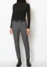 Svart polotröja med lång ärm kombinerad med grå texturerade byxor, åtstramade i midjan med ett svart bälte, och svarta ankellånga stövlar.