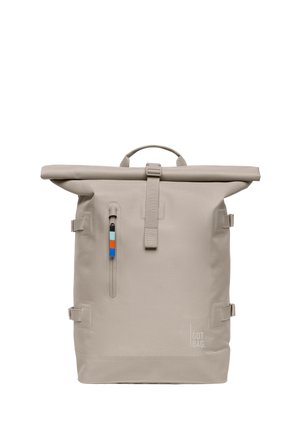 Zaino beige con apertura a rotolo, tasca frontale con cerniera verticale, tiralampo multicolore, cinturini laterali e logo "GOT BAG" in basso a destra.