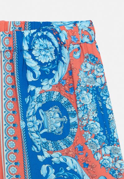 Κοντινή λήψη υφάσματος με κοραλλί και μπλε λουλουδένια και διακοσμητικά πρότυπα, με ένα κεντρικό μπλε στεφάνι με ένα στέμμα μέσα.