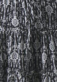Černobílá látka s výraznými vzory zahrnuje složité motivy s vířivými tvary, nashromážděnou texturu a stahovací detail u výstřihu.