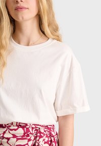 T-shirt bianco in cotone con maniche corte arrotolate, abbinato a una gonna di tessuto a fantasia floreale con tonalità rosa e bianche.