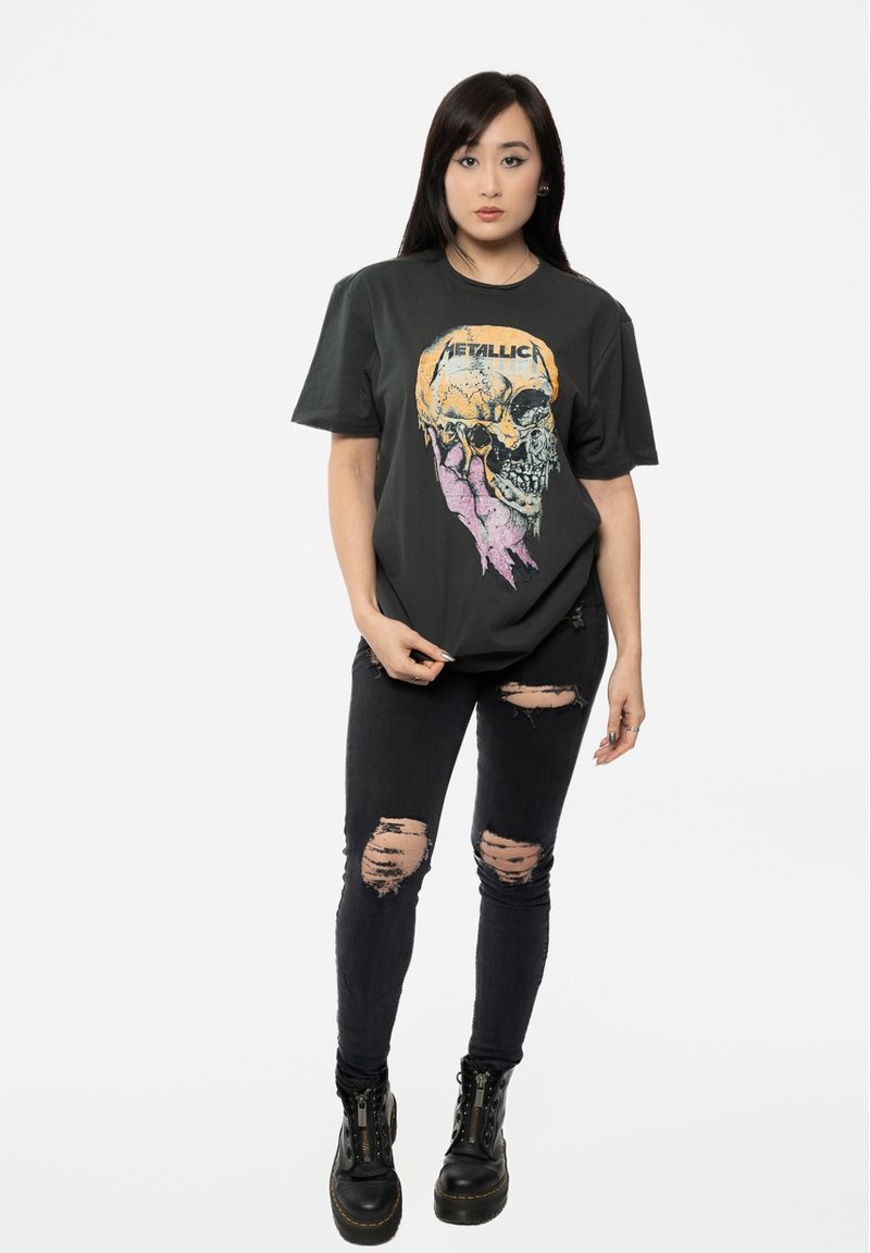 Black graphic t-shirt featuring a skull design in orange and pink. Paired with distressed black jeans and black lace-up boots.