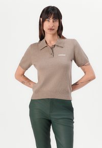 Beige kortärmad polo gjord av mjukt tyg, med en klassisk krage och ribbad fåll. "2ND DAY"-logga broderad på vänster bröst.