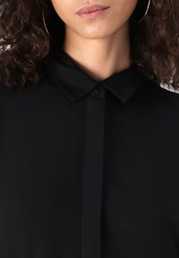Camicia nera con colletto realizzata in tessuto liscio, con patta dei bottoni e design elegante, caratterizzata da una leggera lucentezza e senza motivi visibili.