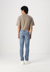 Sivý bavlnený tričko a svetlo modré džínsy, so slim fit strihom, zadnými vreckami a béžovou koženou nášivkou na páse. Biele tenisky.