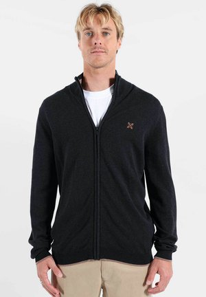 Cardigan gris foncé à fermeture éclair avec col montant, poignets et ourlet côtelés, avec un petit logo sur le côté gauche de la poitrine. Texture de tissu doux.