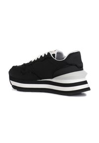 Sneaker nera con tomaia testurizzata, lacci bianchi e suola spessa con strisce bianche e nere. La vista angolata mette in evidenza la differenza di altezza.