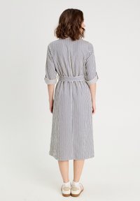 Robe midi rayée avec manches retroussées, en tissu blanc et bleu, ceinturée à la taille, avec une fermeture à boutons à l'avant et des fentes sur les côtés.